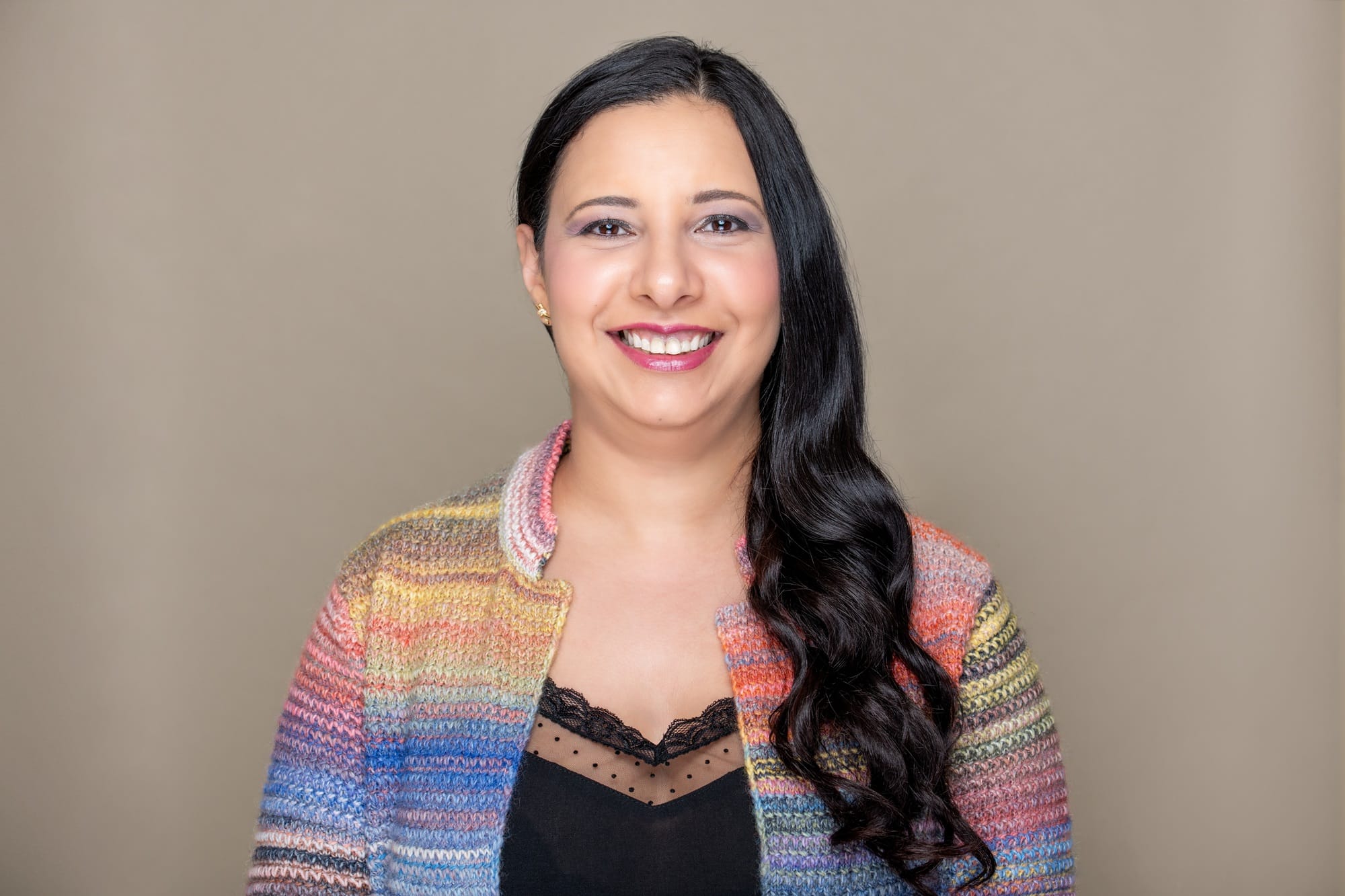 Dr. Marian Masoud, O.D. – Eyeland Eyecare Dr. Marian Masoud, O.D., smiles confidently in a colorful knit jacket against a neutral background – Eyeland Eyecare